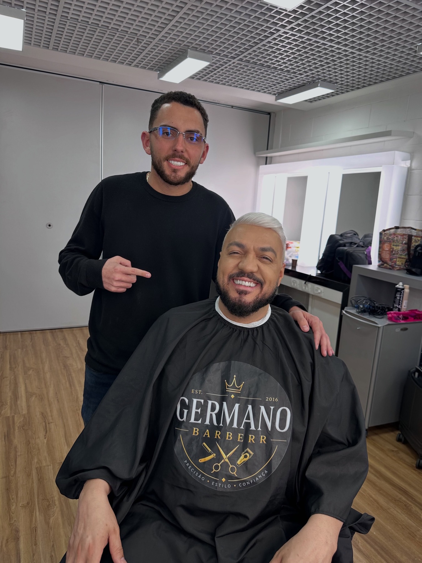 O barbeiro com o cantor Belo na cadeira, usando a capa da Germano Barberr